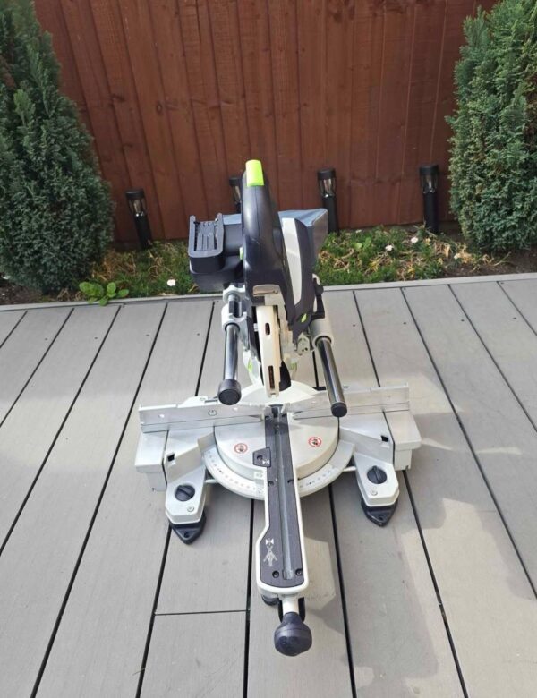 Craftsman using the Festool KAPEX KSC 60 cordless miter saw to make a precise angled cut on a piece of white trim.